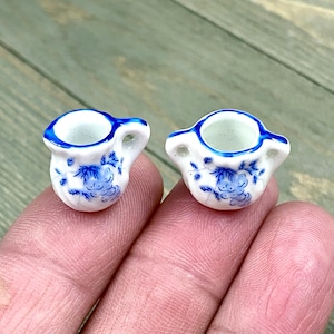 Puede incluir: Dos jarras de cerámica blanca en miniatura con diseños florales azules. Las jarras tienen un solo asa y un cuerpo redondeado.