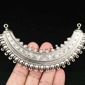 May include: Silver pendant with a crescent moon shape and intricate floral designs. The pendant has a series of small loops along the bottom edge.