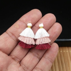 May include: Two tiered tassels in white, pink, and burgundy colors with gold tops.