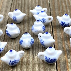 Puede incluir: Una colección de pequeñas teteras de porcelana blanca con diseños florales azules. Cada tetera en miniatura presenta un pico, un asa y una tapa azul. Las teteras están dispuestas sobre una superficie de madera.