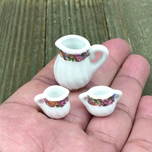 Puede incluir: Un juego de té de porcelana blanca en miniatura con diseños florales. El juego incluye una jarra y dos tazas.