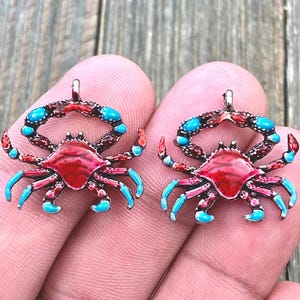 May include: Two red and blue enamel crab charms with silver-tone metal. The crabs have detailed claws and a raised body.