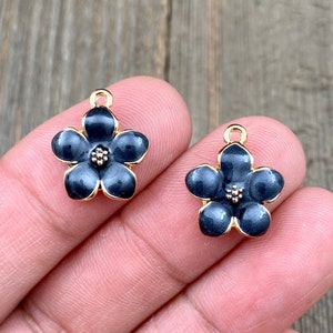 May include: Two gold-tone flower charms with black enamel. Each charm has five petals and a small gold center.