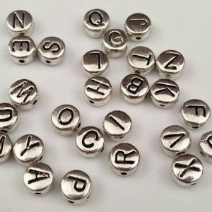 May include: Silver letter beads with black lettering. The beads are round and have a hole in the center. The letters are A, B, C, D, E, F, G, H, I, J, K, L, M, N, O, P, Q, R, S, T, U, V, W, X, Y, and Z.