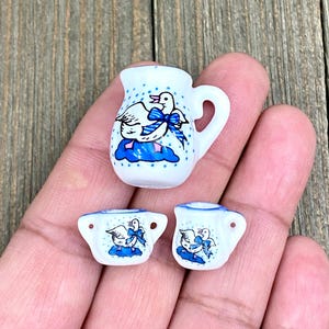 Puede incluir: Un juego de té de cerámica blanca en miniatura con un diseño de ganso azul y blanco. El juego incluye una jarra y dos tazas.