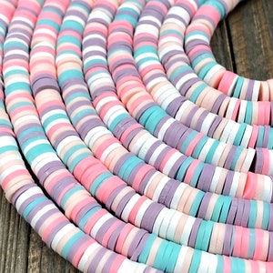 May include: A close-up of a strand of colorful round ceramic beads. The beads are in shades of pink, white, light blue, and purple. The beads are arranged in a repeating pattern.