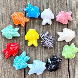 May include: A set of 14 ceramic fish charms in various colors, including blue, green, red, orange, yellow, pink, white, and black. The fish are all different shapes and sizes, and they have a glossy finish.