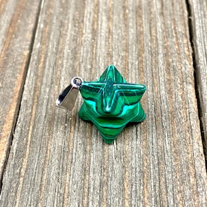 Op de afbeelding: Een groene malachiet ster hanger met een zilveren bedel. De ster is een vijfpuntige ster met een groen en zwart marmerpatroon.