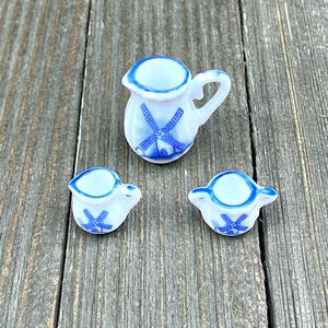 Puede incluir: Un juego de tres jarras de crema y azucareros en miniatura de cerámica con un diseño de molino de viento azul y blanco.