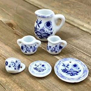 Puede incluir: Un juego de té de porcelana azul y blanco en miniatura con una tetera, una jarra de crema, un azucarero, una taza, un platillo y un plato más grande.