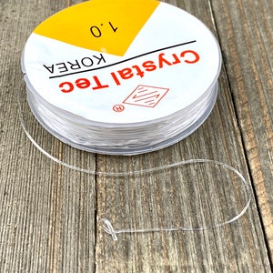 May include: A spool of clear elastic string with a yellow label that reads "Crystal Tec Korea 1.0".