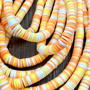May include: A close-up of a strand of colorful polymer clay beads. The beads are round and flat, and they are arranged in a repeating pattern of white, orange, and yellow.