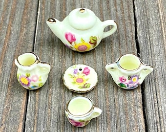 May include: A miniature floral tea set with a teapot, creamer, sugar bowl, cup and saucer. The set is white with gold trim and features a floral pattern in shades of pink, yellow, and purple.