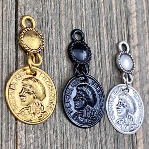 May include: Three gold, silver, and black charm pendants featuring a coin with a profile of a person's face. The coin has the text "REPUBLIQUE FRANCAISE" around the edge.