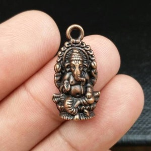 May include: A copper-colored pendant featuring a detailed depiction of the Hindu deity Ganesha. The pendant is intricately designed with Ganesha seated on a lotus throne, holding his traditional attributes.