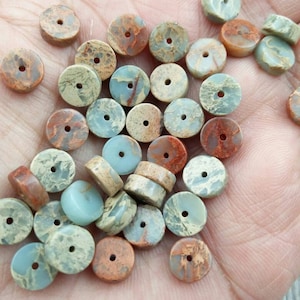 May include: A collection of round, flat, natural stone beads with a hole in the center. The beads are in shades of brown, green, and blue.