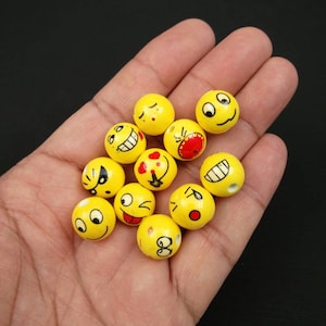 May include: A hand holding a collection of yellow wooden beads with different smiley face expressions painted on them.