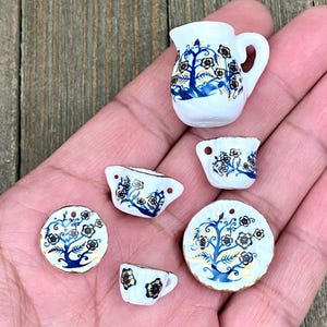 Puede incluir: Un juego de té en miniatura con un diseño floral azul y dorado. El juego incluye una tetera, una jarra de crema, un azucarero, una taza, un platillo y un plato más grande.