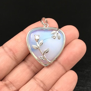 Pode incluir: Um pingente de prata em forma de coração com um delicado design de rosa. O pingente apresenta uma pedra de opala branca com um tom azul claro.