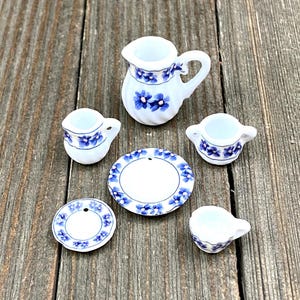 Puede incluir: Un juego de té en miniatura con un patrón floral azul y blanco. El juego incluye una jarra, cuatro tazas, un platillo y un plato.