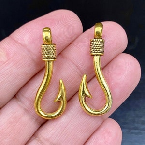 Op de afbeelding: Twee gouden metalen vishaakbedels met een getextureerd ontwerp. De haken zijn ongeveer 5 cm lang.