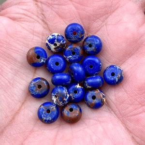 Könnte beinhalten: Eine Sammlung von 18 blauen und braunen marmorierten runden Perlen mit einem Loch in der Mitte. Die Perlen haben einen Durchmesser von etwa 1,2 cm.