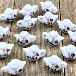 Puede incluir: Una colección de 14 teteras de cerámica blanca con diseños florales. Las teteras son pequeñas y tienen un aspecto delicado.