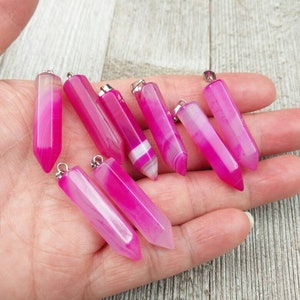 May include: A collection of eight pink and white agate crystal pendants with silver jump rings. The pendants are all in the shape of a long, thin point.