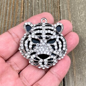 May include: A silver-toned tiger head charm with black enamel eyes and a clear rhinestone design.