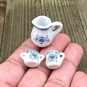 Puede incluir: Un juego de tazas de té de porcelana en miniatura y una jarra con un diseño floral azul y blanco. Las tazas tienen un asa a cada lado y la jarra tiene un asa única.
