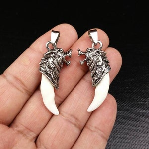 May include: Two silver wolf head pendants with white tooth-shaped charms. The pendants are detailed with intricate designs and are perfect for adding a touch of wildness to any jewelry collection.