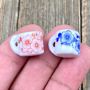 Peut inclure: Deux petites tasses en céramique blanche avec des motifs floraux. Une tasse a un motif floral bleu et l'autre a un motif floral rose.