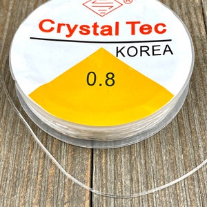 May include: A spool of clear elastic cord with a white label that says "Crystal Tec KOREA" and "0.8".