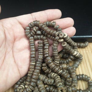 May include: A necklace of dark brown, circular wooden beads. The beads are strung together, creating a decorative item. The beads have a natural, rustic appearance, with visible wood grain.