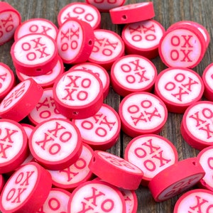 May include: A pile of red and white round beads with the letters "XO" printed on them. The beads are about 1 inch in diameter and have a hole in the center for stringing.