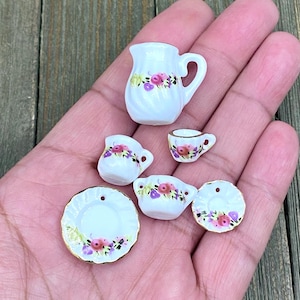 May include: A miniature porcelain tea set with a floral design. The set includes a jug, two cups, two saucers, and a sugar bowl.