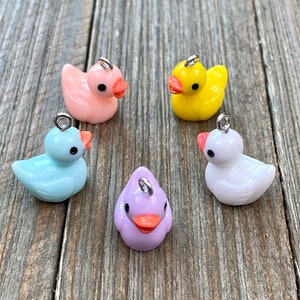 May include: Five small rubber duck charms in different colours: pink, light blue, purple, white and yellow. Each duck has a silver loop for attaching to a necklace or bracelet.