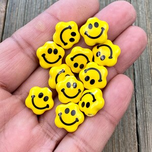 Puede incluir: Una colección de cuentas amarillas con forma de flor con caras sonrientes negras.