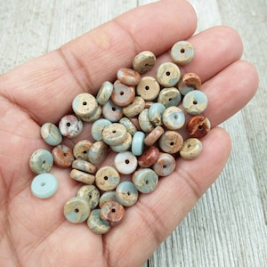 Könnte beinhalten: Eine Sammlung runder, flacher, mehrfarbiger Edelsteinperlen mit einem Loch in der Mitte. Die Perlen sind eine Mischung aus braunen, bräunlichen und hellblauen Farben.