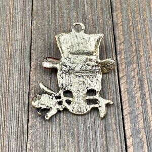May include: Gold-colored metal snowman ornament with a red hat and a twig in each hand. The ornament has a loop at the top for hanging.
