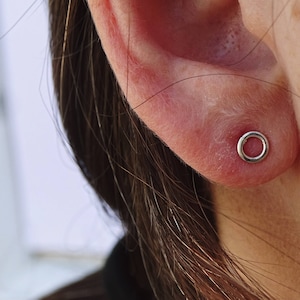 May include: A close-up of a person's ear with a small silver hoop earring. The earring is a simple circle with a smooth finish.