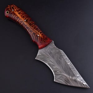 May include: A handcrafted knife with a patterned steel blade and a wooden handle. The handle features a rich, reddish-brown color with lighter wood accents. The blade has a unique, wavy pattern. The knife is designed for cutting.