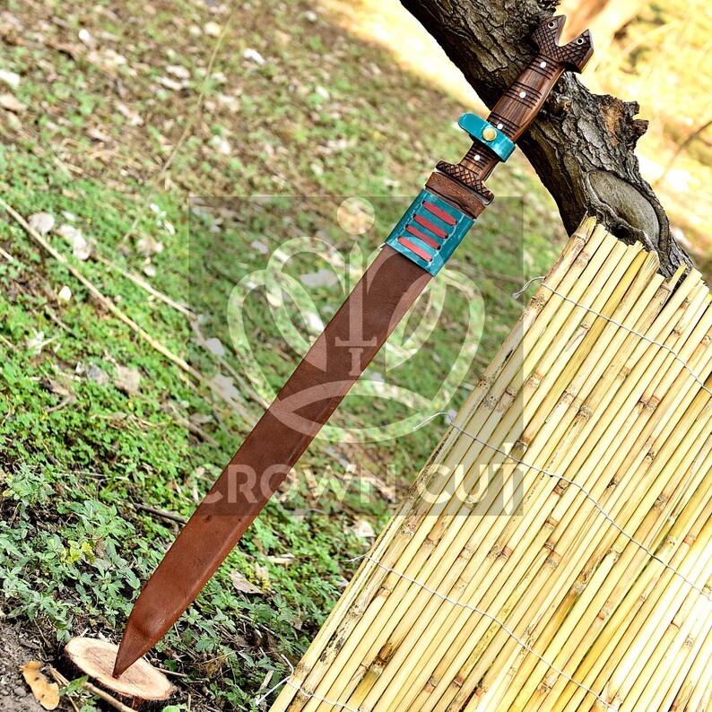 May include: A brown leather-wrapped sword with a turquoise and red patterned handle. The sword is resting on a wooden surface.