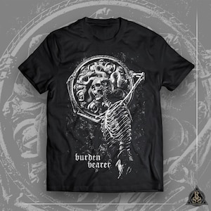 以下が含まれることがあります： 白いグラフィックプリントが施された黒いTシャツ。プリントには、円形のフレームを持った骸骨が描かれており、フレームの中には蛇の頭が入っています。グラフィックの下には「burden bearer」というテキストがプリントされています。