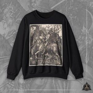 Peut inclure: Sweat-shirt noir avec une illustration vintage d'un chevalier à cheval. L'illustration est en noir et blanc et présente un design détaillé du chevalier, du cheval et des personnages environnants.