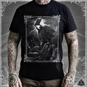 May include: Black t-shirt featuring a graphic print of a man holding two stone tablets. The graphic is in black and white and depicts a dramatic scene with a stormy sky. The text below the graphic reads "Moses Breaking the Tables of the Law".