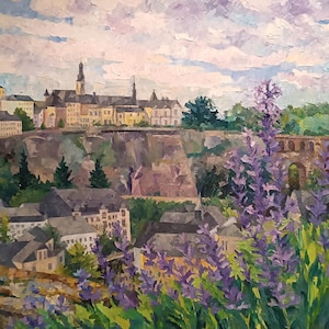 Puede incluir: Pintura al &oacute;leo de un paisaje urbano europeo con edificios y un campanario bajo un cielo nublado. Flores de lavanda en primer plano enmarcan la vista. La pintura utiliza una paleta de morados, verdes y marrones.