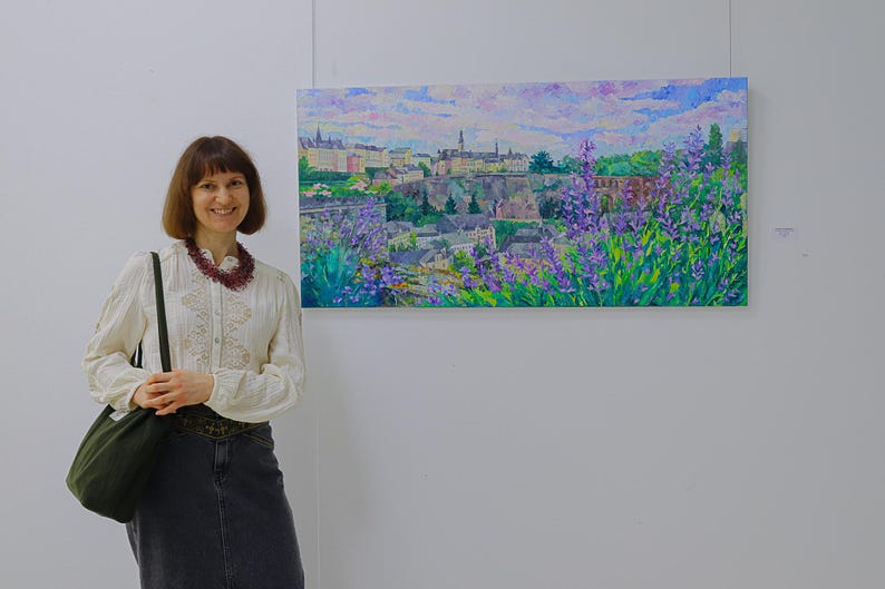 Puede incluir: Una pintura al &oacute;leo de un paisaje urbano con una paleta de colores vibrantes. La obra de arte representa edificios, &aacute;rboles y un cielo nublado, con flores moradas en primer plano. La pintura se exhibe en una pared blanca.