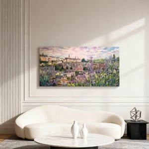 Puede incluir: Una gran pintura rectangular de paisaje representa una ciudad europea con edificios y un cielo vibrante. La pintura cuelga sobre un sof&aacute; blanco curvo, una mesa de centro redonda de m&aacute;rmol y una mesa auxiliar negra. Dos jarrones blancos est&aacute;n sobre la mesa de centro.