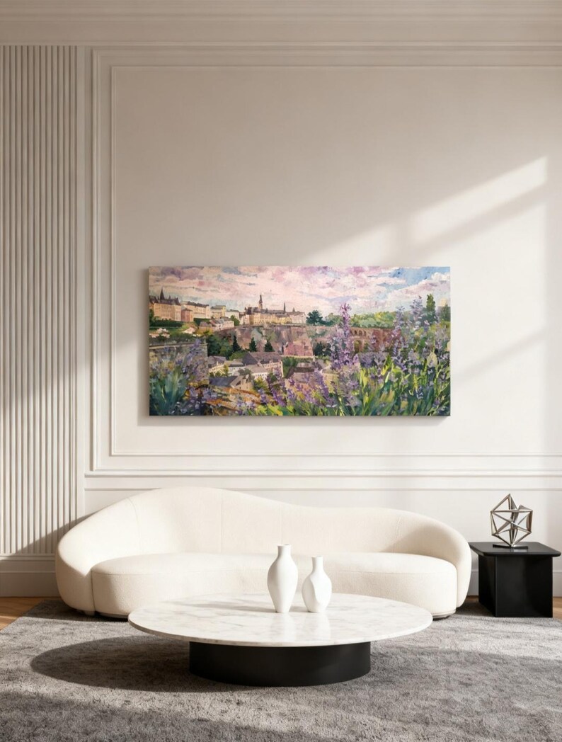 Puede incluir: Una gran pintura rectangular de paisaje representa una ciudad europea con edificios y un cielo vibrante. La pintura cuelga sobre un sof&aacute; blanco curvo, una mesa de centro redonda de m&aacute;rmol y una mesa auxiliar negra. Dos jarrones blancos est&aacute;n sobre la mesa de centro.